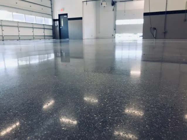 A clean, shiny concrete floor inside a spacious, empty garage with white walls, large windows, and multiple garage doors.