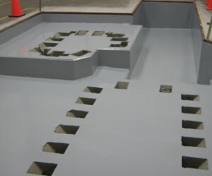 A smooth, gray concrete surface with multiple square and irregularly shaped cutouts is shown; orange traffic cones in the background suggest a construction or renovation area, ideal for new resinous flooring CT installations. A smooth, gray concrete surface with multiple square and irregularly shaped cutouts is shown; orange traffic cones in the background suggest a construction or renovation area, ideal for new resinous flooring CT installations.