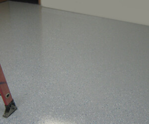 A red ladder stands on a smooth, light gray speckled epoxy flooring Connecticut with a glossy finish. The rest of the room is empty, with a plain wall in the background. A red ladder stands on a smooth, light gray speckled epoxy flooring Connecticut with a glossy finish. The rest of the room is empty, with a plain wall in the background.