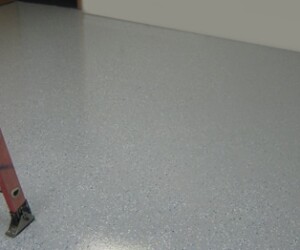 A red ladder stands on a smooth, light gray speckled epoxy flooring Connecticut with a glossy finish. The rest of the room is empty, with a plain wall in the background. A red ladder stands on a smooth, light gray speckled epoxy flooring Connecticut with a glossy finish. The rest of the room is empty, with a plain wall in the background.