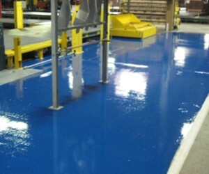 A shiny blue epoxy-coated floor in an industrial setting, perfect for commercial kitchen flooring, with metal support structures and yellow equipment visible in the background. A shiny blue epoxy-coated floor in an industrial setting, perfect for commercial kitchen flooring, with metal support structures and yellow equipment visible in the background.