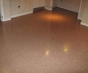 A room with a smooth, shiny, light brown industrial floor coating, beige walls, and white baseboards; electrical outlets and some unfinished areas are visible. A room with a smooth, shiny, light brown industrial floor coating, beige walls, and white baseboards; electrical outlets and some unfinished areas are visible.