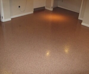 A room with a smooth, shiny, light brown industrial floor coating, beige walls, and white baseboards; electrical outlets and some unfinished areas are visible. A room with a smooth, shiny, light brown industrial floor coating, beige walls, and white baseboards; electrical outlets and some unfinished areas are visible.