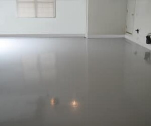 A clean, empty room with a smooth, shiny gray anti-slip epoxy floor, white walls, a window with blinds, and a closed door. A clean, empty room with a smooth, shiny gray anti-slip epoxy floor, white walls, a window with blinds, and a closed door.