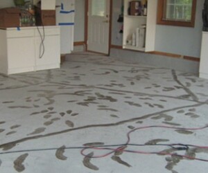 A garage floor with dirty footprints and mud tracks scattered across the concrete surface. Boxes and cabinets are visible along the walls, and electrical cords are lying on the USDA approved flooring. A garage floor with dirty footprints and mud tracks scattered across the concrete surface. Boxes and cabinets are visible along the walls, and electrical cords are lying on the USDA approved flooring.