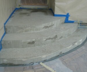 Three newly poured concrete steps are partially dried, surrounded by blue painter’s tape and plastic sheeting for protection. The area is prepared for further construction or finishing work, possibly including USDA approved flooring installation. Three newly poured concrete steps are partially dried, surrounded by blue painter’s tape and plastic sheeting for protection. The area is prepared for further construction or finishing work, possibly including USDA approved flooring installation.
