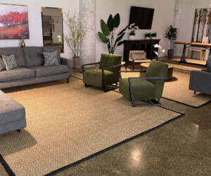 A modern living room with gray sofas, green armchairs, a woven rug, lush plants, and wall art features polished concrete floors finished with anti-slip epoxy floor coating and bold white columns for an industrial yet inviting vibe. A modern living room with gray sofas, green armchairs, a woven rug, lush plants, and wall art features polished concrete floors finished with anti-slip epoxy floor coating and bold white columns for an industrial yet inviting vibe.