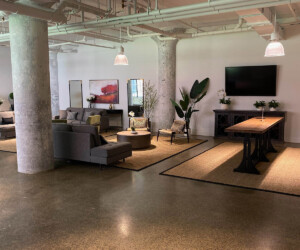 Modern lounge area with gray sofas, a large TV, long wooden tables, plants, and exposed concrete columns under hanging lights; anti-slip epoxy floor enhances safety while the minimalist decor creates an open, stylish setting. Modern lounge area with gray sofas, a large TV, long wooden tables, plants, and exposed concrete columns under hanging lights; anti-slip epoxy floor enhances safety while the minimalist decor creates an open, stylish setting.