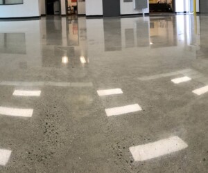 A wide, empty industrial room with polished concrete or epoxy flooring Connecticut reflecting overhead lights and windows. The space has white walls, some doors, and large open areas. A wide, empty industrial room with polished concrete or epoxy flooring Connecticut reflecting overhead lights and windows. The space has white walls, some doors, and large open areas.