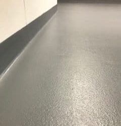 Textured gray epoxy flooring Connecticut with coved edges rises slightly up the white walls, creating a clean, seamless look ideal for commercial kitchen flooring in any indoor space. Textured gray epoxy flooring Connecticut with coved edges rises slightly up the white walls, creating a clean, seamless look ideal for commercial kitchen flooring in any indoor space.