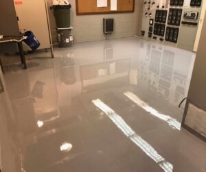 A clean, shiny, gray anti-slip epoxy floor in a utility or electrical control room with various panels, cabinets, and equipment along the walls. A clean, shiny, gray anti-slip epoxy floor in a utility or electrical control room with various panels, cabinets, and equipment along the walls.