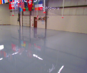 A large, empty indoor space with a shiny, USDA approved flooring; various international flags hang from the ceiling, and there are beige walls and doors in the background. A large, empty indoor space with a shiny, USDA approved flooring; various international flags hang from the ceiling, and there are beige walls and doors in the background.