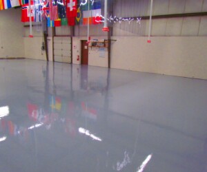 A large, empty indoor space with a shiny, USDA approved flooring; various international flags hang from the ceiling, and there are beige walls and doors in the background. A large, empty indoor space with a shiny, USDA approved flooring; various international flags hang from the ceiling, and there are beige walls and doors in the background.