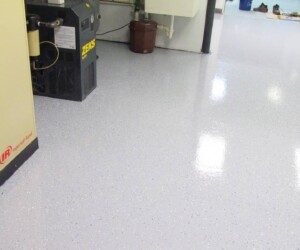 A clean, shiny, light gray speckled anti-slip epoxy floor in an industrial room, with machinery and equipment visible in the background. A clean, shiny, light gray speckled anti-slip epoxy floor in an industrial room, with machinery and equipment visible in the background.
