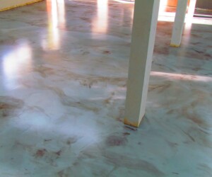 A room with a glossy, marbled anti-slip epoxy floor in shades of grey and brown, illuminated by sunlight streaming through windows. White pillars stand on the floor, and the edges are taped for protection. A room with a glossy, marbled anti-slip epoxy floor in shades of grey and brown, illuminated by sunlight streaming through windows. White pillars stand on the floor, and the edges are taped for protection.