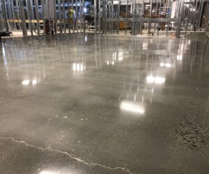 A polished concrete floor reflecting ceiling lights in a building under construction, with exposed metal wall framing and construction materials visible in the background—ideal for commercial kitchen flooring or USDA approved flooring solutions. A polished concrete floor reflecting ceiling lights in a building under construction, with exposed metal wall framing and construction materials visible in the background—ideal for commercial kitchen flooring or USDA approved flooring solutions.