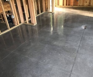 A room under construction features exposed wooden wall framing and a smooth, shiny, polished concrete floor marked with large square sections—ideal for an industrial floor coating or anti-slip epoxy floor installation. A room under construction features exposed wooden wall framing and a smooth, shiny, polished concrete floor marked with large square sections—ideal for an industrial floor coating or anti-slip epoxy floor installation.