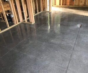 A room under construction features exposed wooden wall framing and a smooth, shiny, polished concrete floor marked with large square sections—ideal for an industrial floor coating or anti-slip epoxy floor installation. A room under construction features exposed wooden wall framing and a smooth, shiny, polished concrete floor marked with large square sections—ideal for an industrial floor coating or anti-slip epoxy floor installation.