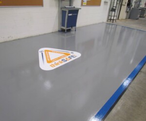 A clean, shiny industrial floor with a triangular safety sign that reads thinkSAFE and INCIDENT, INJURY, NEAR MISS stands next to a workstation against a white wall, showcasing durable epoxy flooring Connecticut businesses trust. A clean, shiny industrial floor with a triangular safety sign that reads thinkSAFE and INCIDENT, INJURY, NEAR MISS stands next to a workstation against a white wall, showcasing durable epoxy flooring Connecticut businesses trust.