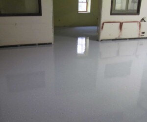 A room with freshly applied, glossy light gray epoxy flooring Connecticut, reflecting the surrounding walls and windows. The unfinished walls show some patches and marks, highlighting the contrast with the sleek industrial floor coating. A room with freshly applied, glossy light gray epoxy flooring Connecticut, reflecting the surrounding walls and windows. The unfinished walls show some patches and marks, highlighting the contrast with the sleek industrial floor coating.