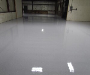 A large indoor industrial space with smooth, glossy, light gray epoxy flooring Connecticut reflecting overhead lights. The white walls and pristine, empty area highlight the durability and appeal of resinous flooring CT. A large indoor industrial space with smooth, glossy, light gray epoxy flooring Connecticut reflecting overhead lights. The white walls and pristine, empty area highlight the durability and appeal of resinous flooring CT.