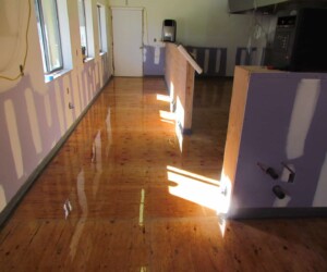 A room with unfinished walls and exposed drywall has water pooled on the shiny wooden floor, reflecting sunlight coming through the windows. A counter and some kitchen equipment are visible, suggesting the need for commercial kitchen flooring. A room with unfinished walls and exposed drywall has water pooled on the shiny wooden floor, reflecting sunlight coming through the windows. A counter and some kitchen equipment are visible, suggesting the need for commercial kitchen flooring.