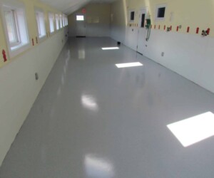 A long, clean hallway with shiny resinous flooring CT in light gray, white lower walls, and several windows on the left. Small red figurines line the window sill as sunlight streams through, highlighting the durable industrial floor coating. A long, clean hallway with shiny resinous flooring CT in light gray, white lower walls, and several windows on the left. Small red figurines line the window sill as sunlight streams through, highlighting the durable industrial floor coating.