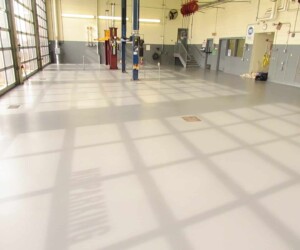 A clean, empty auto service garage with a shiny, resinous flooring CT finish, tall windows casting grid-like shadows, car lifts, wall-mounted equipment, and stairs leading to an upper area in the background. A clean, empty auto service garage with a shiny, resinous flooring CT finish, tall windows casting grid-like shadows, car lifts, wall-mounted equipment, and stairs leading to an upper area in the background.