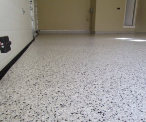 Close-up view of a clean, speckled anti-slip epoxy floor with beige walls and a partially visible garage door on the left. Sunlight streams through a window, highlighting the durability and style of epoxy flooring Connecticut homes love. Close-up view of a clean, speckled anti-slip epoxy floor with beige walls and a partially visible garage door on the left. Sunlight streams through a window, highlighting the durability and style of epoxy flooring Connecticut homes love.