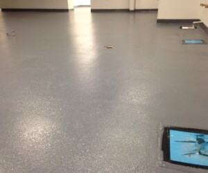 A smooth, grey, freshly coated anti-slip epoxy floor in an empty room with a few exposed drains and utility openings. The white walls and minimal fixtures make it ideal for commercial kitchen flooring in Connecticut. A smooth, grey, freshly coated anti-slip epoxy floor in an empty room with a few exposed drains and utility openings. The white walls and minimal fixtures make it ideal for commercial kitchen flooring in Connecticut.