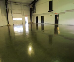 A large, empty industrial warehouse with high white walls, black doors, and overhead lighting reflecting on polished resinous flooring CT for a sleek, modern look. A large, empty industrial warehouse with high white walls, black doors, and overhead lighting reflecting on polished resinous flooring CT for a sleek, modern look.