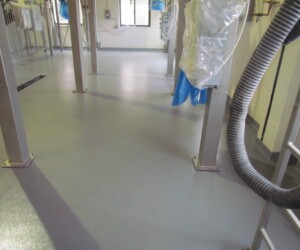 A clean industrial room with a smooth, gray epoxy flooring Connecticut floor, metal support beams, hanging hoses, pipes, and equipment. Sunlight enters through windows in the back, illuminating the tidy, uncluttered space. A clean industrial room with a smooth, gray epoxy flooring Connecticut floor, metal support beams, hanging hoses, pipes, and equipment. Sunlight enters through windows in the back, illuminating the tidy, uncluttered space.