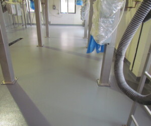 A clean industrial room with a smooth, gray epoxy flooring Connecticut floor, metal support beams, hanging hoses, pipes, and equipment. Sunlight enters through windows in the back, illuminating the tidy, uncluttered space. A clean industrial room with a smooth, gray epoxy flooring Connecticut floor, metal support beams, hanging hoses, pipes, and equipment. Sunlight enters through windows in the back, illuminating the tidy, uncluttered space.