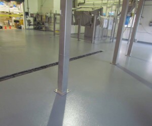 A clean industrial or factory space with a smooth gray USDA approved flooring, metal support columns, machinery, storage bags, and equipment visible in the background. A clean industrial or factory space with a smooth gray USDA approved flooring, metal support columns, machinery, storage bags, and equipment visible in the background.