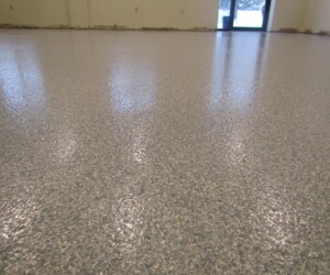 A close-up view of a shiny, speckled anti-slip epoxy floor in an empty room with beige walls and minimal light reflecting off the surface—a durable choice for commercial kitchen flooring. A close-up view of a shiny, speckled anti-slip epoxy floor in an empty room with beige walls and minimal light reflecting off the surface—a durable choice for commercial kitchen flooring.
