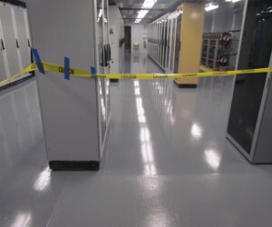 A server room with shiny anti-slip epoxy flooring has a section blocked off by yellow caution tape attached to columns, indicating restricted access or ongoing maintenance. A server room with shiny anti-slip epoxy flooring has a section blocked off by yellow caution tape attached to columns, indicating restricted access or ongoing maintenance.