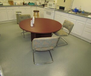 A round wooden table with three cushioned chairs sits in the center of a kitchen featuring white cabinets, a microwave, and a stool, all set atop an anti-slip epoxy floor for added safety and style. A round wooden table with three cushioned chairs sits in the center of a kitchen featuring white cabinets, a microwave, and a stool, all set atop an anti-slip epoxy floor for added safety and style.