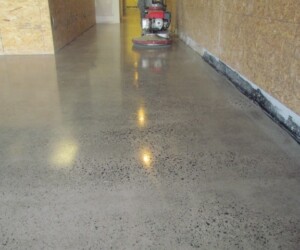 A hallway with polished concrete flooring, reflecting overhead lights. A floor polishing machine is visible in the background near the end of the hallway. The walls are unfinished, with exposed wooden panels on the right side—ideal for epoxy flooring Connecticut. A hallway with polished concrete flooring, reflecting overhead lights. A floor polishing machine is visible in the background near the end of the hallway. The walls are unfinished, with exposed wooden panels on the right side—ideal for epoxy flooring Connecticut.