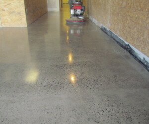 A hallway with polished concrete flooring, reflecting overhead lights. A floor polishing machine is visible in the background near the end of the hallway. The walls are unfinished, with exposed wooden panels on the right side—ideal for epoxy flooring Connecticut. A hallway with polished concrete flooring, reflecting overhead lights. A floor polishing machine is visible in the background near the end of the hallway. The walls are unfinished, with exposed wooden panels on the right side—ideal for epoxy flooring Connecticut.