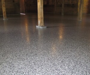 A spacious room with wooden support beams and a smooth, glossy, speckled gray anti-slip epoxy floor reflecting light from above. A spacious room with wooden support beams and a smooth, glossy, speckled gray anti-slip epoxy floor reflecting light from above.