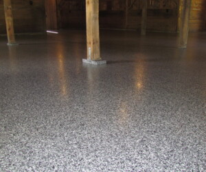 A spacious room with wooden support beams and a smooth, glossy, speckled gray anti-slip epoxy floor reflecting light from above. A spacious room with wooden support beams and a smooth, glossy, speckled gray anti-slip epoxy floor reflecting light from above.