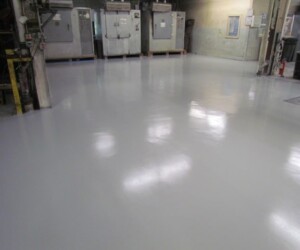 A large industrial room with a smooth, shiny, light gray anti-slip epoxy floor, surrounded by industrial equipment and machines along the walls. A large industrial room with a smooth, shiny, light gray anti-slip epoxy floor, surrounded by industrial equipment and machines along the walls.