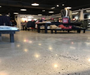 Clothing store interior with neatly folded clothes on black tables, racks of hanging garments, sale signs offering 50% off, and mannequins dressed in casual outfits under ceiling lights. Features a polished anti-slip epoxy floor. Clothing store interior with neatly folded clothes on black tables, racks of hanging garments, sale signs offering 50% off, and mannequins dressed in casual outfits under ceiling lights. Features a polished anti-slip epoxy floor.