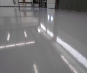 A close-up view of a smooth, shiny, light gray epoxy-coated floor, reflecting overhead lights and parts of the room’s interior—ideal for commercial kitchen flooring with durable, USDA approved flooring standards. A close-up view of a smooth, shiny, light gray epoxy-coated floor, reflecting overhead lights and parts of the room’s interior—ideal for commercial kitchen flooring with durable, USDA approved flooring standards.
