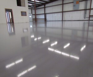 Interior of an empty industrial warehouse with smooth, glossy gray epoxy flooring Connecticut residents trust, reflecting overhead fluorescent lights. The space has white walls, exposed beams, and a small office area in the corner. Interior of an empty industrial warehouse with smooth, glossy gray epoxy flooring Connecticut residents trust, reflecting overhead fluorescent lights. The space has white walls, exposed beams, and a small office area in the corner.