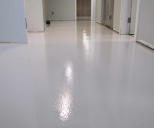 A hallway with freshly painted, glossy white floors features industrial floor coating, surrounded by white walls and doors, with a clear reflection visible on the surface. A hallway with freshly painted, glossy white floors features industrial floor coating, surrounded by white walls and doors, with a clear reflection visible on the surface.