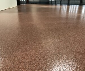 A close-up view of a smooth, shiny brown industrial floor coating inside a large commercial building, with visible walls and distant doors. A close-up view of a smooth, shiny brown industrial floor coating inside a large commercial building, with visible walls and distant doors.