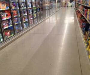 A grocery store aisle with freezers stocked with food on the left and shelves filled with packaged goods on the right; the shiny USDA approved flooring is spotless and empty. A grocery store aisle with freezers stocked with food on the left and shelves filled with packaged goods on the right; the shiny USDA approved flooring is spotless and empty.
