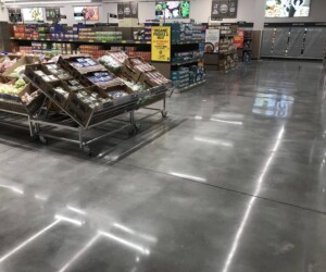 A grocery store with produce and packaged foods on racks to the left, refrigerated sections with glass doors along the back and right walls, and a shiny anti-slip epoxy floor that keeps the clean, organized space safe for shoppers. A grocery store with produce and packaged foods on racks to the left, refrigerated sections with glass doors along the back and right walls, and a shiny anti-slip epoxy floor that keeps the clean, organized space safe for shoppers.
