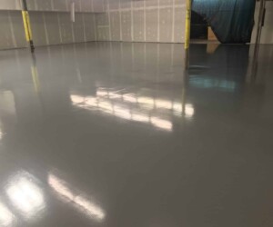 A large indoor space with freshly installed, shiny gray epoxy flooring; unfinished walls with exposed drywall and pillars are visible, and bright lights reflect off the smooth surface—perfect for those seeking premium epoxy flooring Connecticut. A large indoor space with freshly installed, shiny gray epoxy flooring; unfinished walls with exposed drywall and pillars are visible, and bright lights reflect off the smooth surface—perfect for those seeking premium epoxy flooring Connecticut.